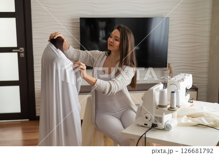 Caucasian woman sews a dress at home. Workspace of a seamstress Caucasian woman sews a dress at home. Workspace of a seamstress 126681792