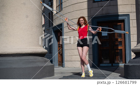 Young red-haired woman in shorts moves with crutches outdoors. Young red-haired woman in shorts moves with crutches outdoors. 126681799