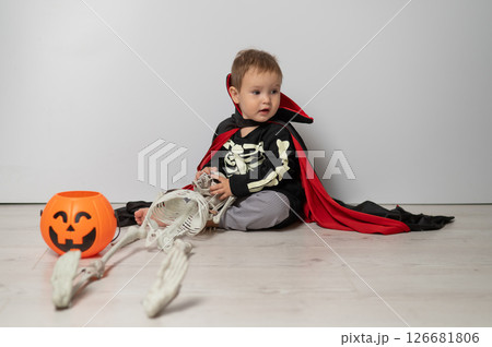 Little Caucasian boy in Dracula costume holding skull on white background.  126681806