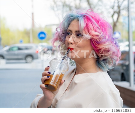 Close-up portrait of curly Caucasian woman with multi-colored hair wearing glasses. The hairstyle model is drinking a cold drink Close-up portrait of curly Caucasian woman with multi-colored hair wearing glasses. The hairstyle model is drinking a cold drink 126681882