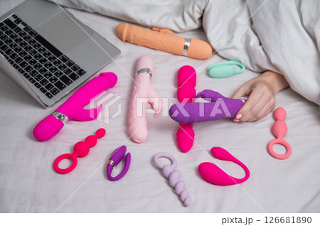 Woman holding sex toy. Various vibrators and laptop on bed. Woman holding sex toy. Various vibrators and laptop on bed. 126681890