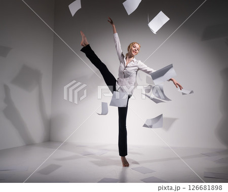 A graceful ballerina in a business suit throws documents. Business woman dance barefoot on a white background A graceful ballerina in a business suit throws documents. Business woman dance barefoot on a white background 126681898