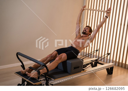 A man doing Pilates on a reformer. A man doing Pilates on a reformer. 126682095