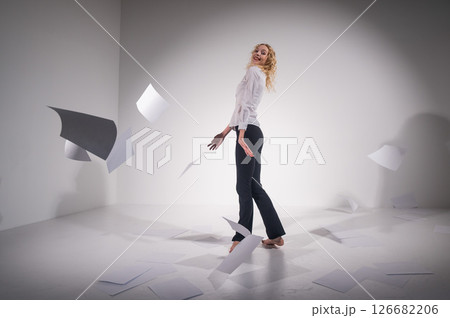 A graceful ballerina in a business suit throws documents. Business woman dance barefoot on a white background A graceful ballerina in a business suit throws documents. Business woman dance barefoot on a white background 126682206