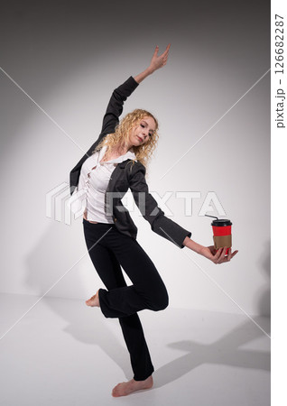 Barefoot ballerina in business suit jumping with a cup of coffee on a white background.  126682287