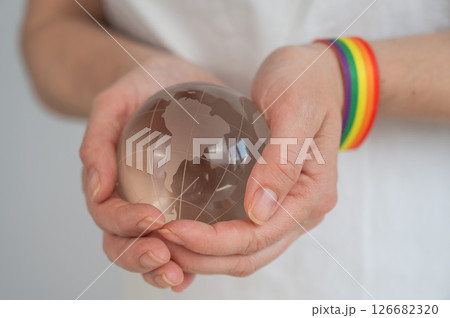 Woman wearing rainbow flag bracelet holding glass globe.  126682320