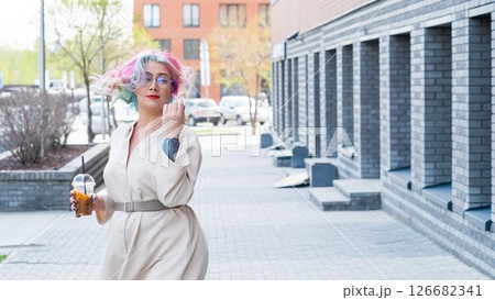 Close-up portrait of curly Caucasian woman with multi-colored hair wearing glasses. The hairstyle model is drinking a cold drink 126682341