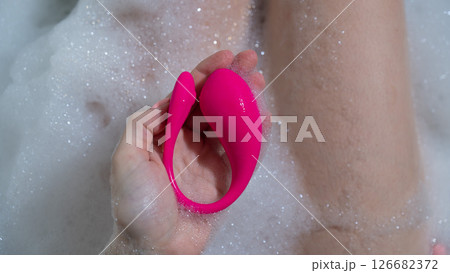A woman lies in a bubble bath and holds a curved pink vibrator. 126682372