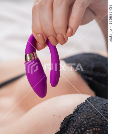 Woman lying in lace lingerie holding curved pink vibrator.  126682455