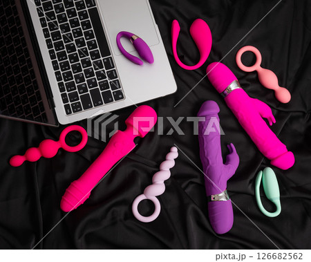 Collection of sex toys on a black sheet. Top view of various vibrators and a laptop. Collection of sex toys on a black sheet. Top view of various vibrators and a laptop. 126682562