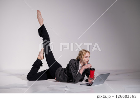 A ballerina dressed in a business suit poses for a laptop and drinks coffee. Flexible woman works at the computer A ballerina dressed in a business suit poses for a laptop and drinks coffee. Flexible woman works at the computer 126682565