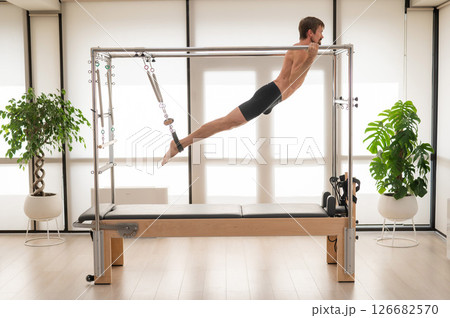 A man performs aerial exercises on a reformer machine. 126682570