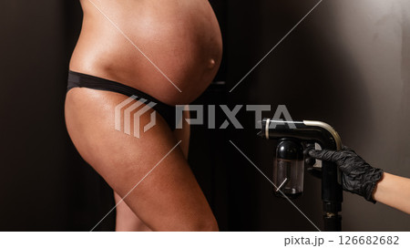 Faceless pregnant woman getting an instant tan. The master applies bronzer with a spray. Faceless pregnant woman getting an instant tan. The master applies bronzer with a spray. 126682682