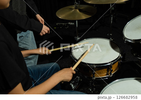 Young caucasian woman teaches a boy to play the drums in the studio on a black background. Music school student 126682958