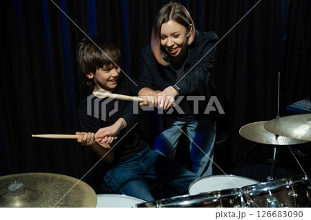 Young caucasian woman teaches a boy to play the drums in the studio on a black background. Music school student 126683090