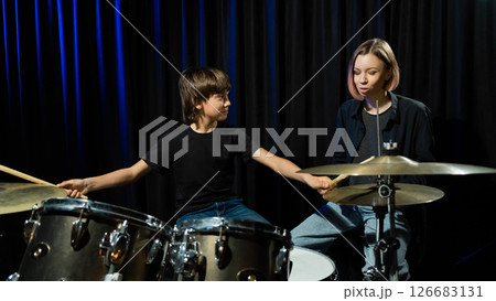 Young caucasian woman teaches a boy to play the drums in the studio on a black background. Music school student Young caucasian woman teaches a boy to play the drums in the studio on a black background. Music school student 126683131