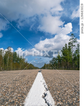 Wide open road stretches through a forest under a blue sky with fluffy clouds on a clear sunny day Wide open road stretches through a forest under a blue sky with fluffy clouds on a clear sunny day 126683819