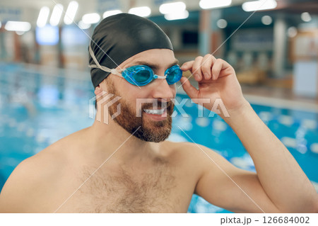 Well-built young man in swimming cap in the pool looking contented Well-built young man in swimming cap in the pool looking contented 126684002