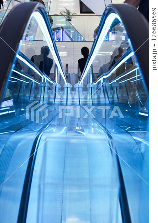 Brightly lit escalator features blue lighting in a busy shopping center. 126686569