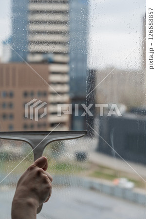 A woman washes a window with a scraper.  126688857