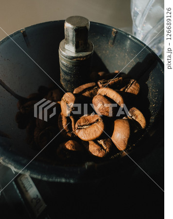 Roasted coffee beans resting inside dark grinder, waiting to be transformed into aromatic coffee powder, filling air with rich, invigorating aromas perfect for brewing. Dark grinder, coffee beans 126689126