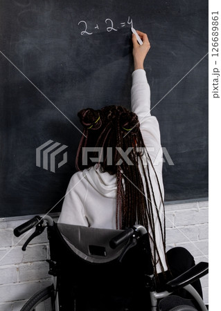 An empowered educator shares their knowledge by writing on a chalkboard while in a wheelchair 126689861