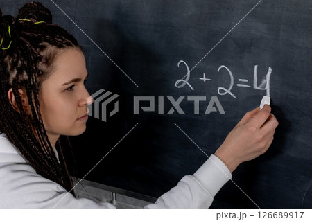A dedicated student diligently solving a complex math equation on a chalkboard in class A dedicated student diligently solving a complex math equation on a chalkboard in class 126689917