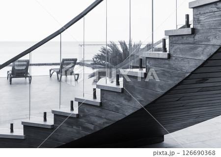 Elegant wooden staircase with glass railing overlooking a beachside patio 126690368