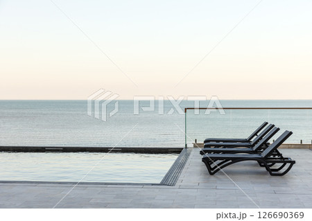 Relaxing ocean view with a modern infinity pool and lounge chairs Relaxing ocean view with a modern infinity pool and lounge chairs 126690369