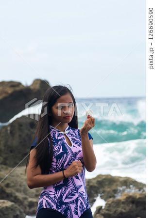 young asian woman shows off white round pebble found on pebble beach near tropical sea 126690590