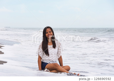 Happy woman sitting on the beach with waves in the background 126690592