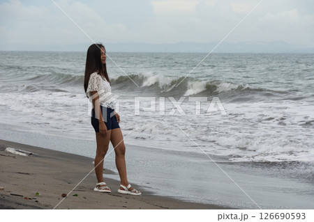 Confident woman standing on beach near sea waves Confident woman standing on beach near sea waves 126690593