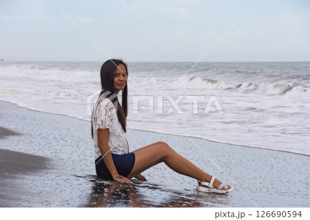 young woman sitting on wet black sand beach near waves young woman sitting on wet black sand beach near waves 126690594