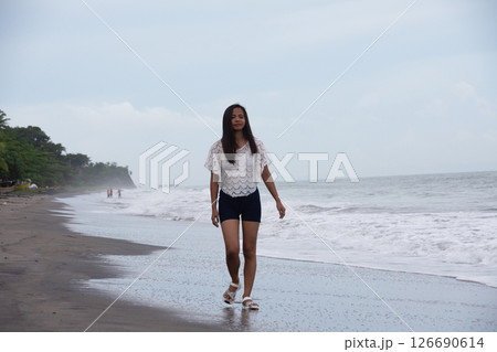 Confident young woman walking alone on the beach near the sea waves Confident young woman walking alone on the beach near the sea waves 126690614