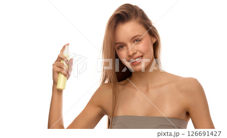 Attractive woman with wet hair holding hair spray bottle and smiling at camera, showing part of beauty ritual and product use for moisture and styling Attractive woman with wet hair holding hair spray bottle and smiling at camera, showing part of beauty ritual and product use for moisture and styling 126691427