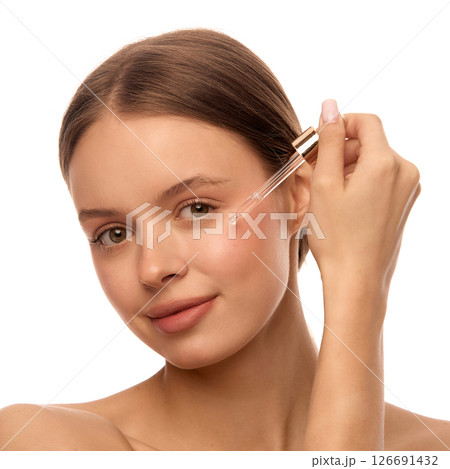 Close-up portrait of woman applying cosmetic serum with glass dropper to under eye area, show skincare and daily face care routine 126691432