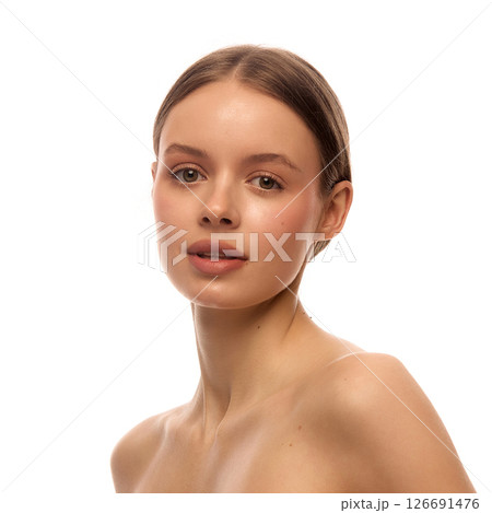 Beautiful young woman looks at camera with clear skin, with slight smile, shiny eyes and neutral makeup against white background Beautiful young woman looks at camera with clear skin, with slight smile, shiny eyes and neutral makeup against white background 126691476