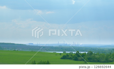 Expansive Lush Green Fields with a Distinct Industrial Background Beneath a Cloudy Sky Time lapse. Expansive Lush Green Fields with a Distinct Industrial Background Beneath a Cloudy Sky Time lapse. 126692644