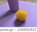 Yellow massage ball in close-up on the background of a roll for myofascial relaxation lying on a fitness and yoga mat. Sports equipment is lying on the wooden floor 126692825