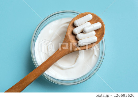 Probiotic capsules and bowl of yogurt on blue 126693626