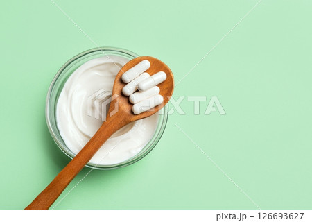 Probiotic capsules and bowl of yogurt on green 126693627