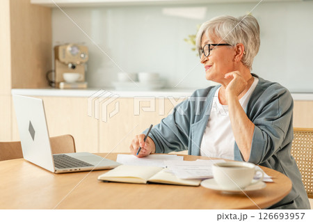 Middle aged senior woman using laptop computer writing notes at home. Focused mature old businesswoman work in home office making written records doing online work. Mature boss professional worker Middle aged senior woman using laptop computer writing notes at home. Focused mature old businesswoman work in home office making written records doing online work. Mature boss professional worker 126693957
