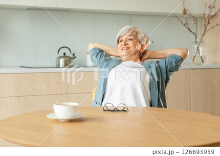 Senior old woman feeling relaxed stretching arms in kitchen at home. Smiling mature woman stretching hands feel positive optimistic fresh on bright morning new day. Good mood happy elderly lifestyle Senior old woman feeling relaxed stretching arms in kitchen at home. Smiling mature woman stretching hands feel positive optimistic fresh on bright morning new day. Good mood happy elderly lifestyle 126693959