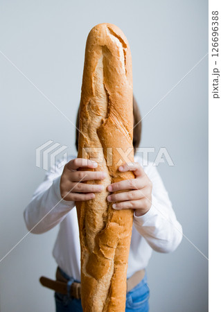 Child holding large baguette loaf in front of face with white background Child holding large baguette loaf in front of face with white background 126696388