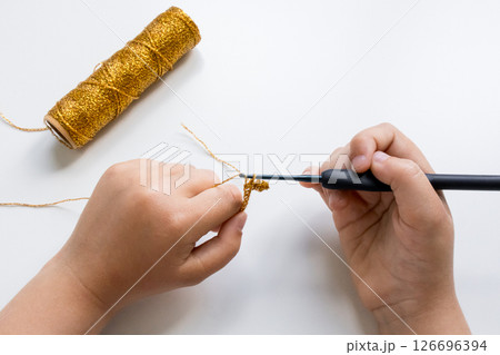 Child crocheting with gold yarn and hook on white surface close up 126696394