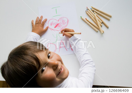 Hispanic child drawing father day card with heart design on white paper Hispanic child drawing father day card with heart design on white paper 126696409