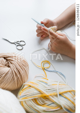 Child crocheting with yarn and scissors on white surface 126696411
