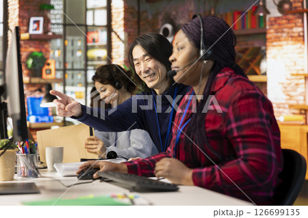 Happy customer service senior manager teaching new employee how to track support tickets in company software. Cheerful Asian call center supervisor shows intern how to create and close support tickets 126699135