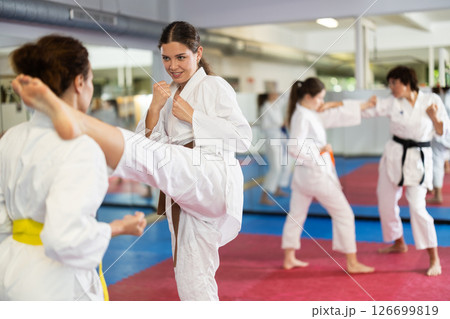 Womens practicing new karate moves in pairs in class with trainer 126699819