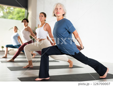 Woman with group of adult people doing stretching workout for body flexibility in yoga studio 126700007